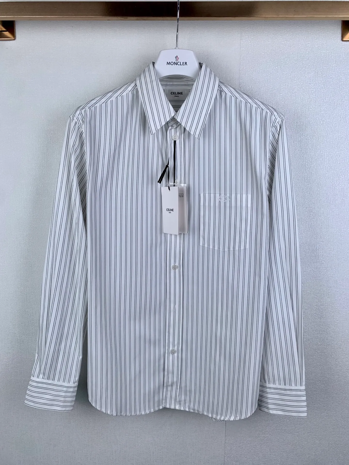 Celine Black White striped Arc de Triomphe logo embroidered long-sleeved shirt Fabric selection: Made of 100% natural cotton fiber without any chemical fiber blending to ensure the purity of the fabric from the source. The hollow structure inside the cotton fiber forms a natural "air channel", making the fabric excellent breathability. Air can freely circulate through the gaps between the fibers, quickly discharging moisture and heat from the body surface, keeping you dry even if you wear it for a long time, and avoiding the stuffy and sticky feeling. At the same time, its hygroscopicity is much higher than that of synthetic fibers. When the human body sweats, the fabric can quickly absorb the sweat and spread it to the surface, accelerating evaporation through air flow, achieving a dynamic balance of "moisture absorption-release" and keeping the skin dry and comfortable. Embroidery technology: The embroidery machine uses cotton thread to outline the logo, and the stitches are fine and even, ensuring smooth and clear lines and forming a full three-dimensional texture. The embroidery area is about 3.5×2.3cm, and the edges are narrowed with "overlock embroidery" to prevent the yarn from loosening and enhance the three-dimensionality and durability of the pattern. The logo pattern is presented in miniature flat embroidery. The height of the finished product is only 0.1cm, but it is clearly legible. Ironing details: The ironer turns the collar up, irons it from the bottom to the top using high-temperature and moist steam, applies pressure to smooth out the wrinkles, and then turns it over to the front and repeats the operation. Turn to the neckline and iron it into an arc shape, and press the back collar to the bottom to keep it straight. The rotator cuff part uses the hanging method to avoid crushing the edges. After adjusting the fiber density through the ironer's "push, return, and pull" technique, the shirt can better fit the body curve. Accessories: One-to-one customized buttons One-to-one customized three-label Size: 46 48 50 52